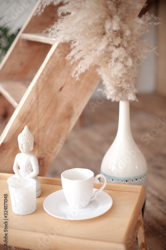 Breakfast set close up in the room. Coffee cup on a tray with statuette decoration. Selective focus. Boho style