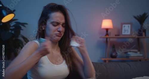 Close up of young unhappy woman tearing angrily photo and throwing away while sitting on sofa. Sad girl crying and putting hand on face after painful brokeup with lover.