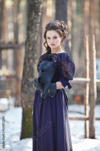 A girl walks through the winter forest with a raven in her hand.