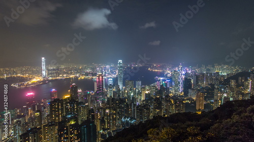 Hong Kong city skyline timelapse at night with Victoria Harbor and skyscrapers illuminated by lights over water viewed from mountain top. © neiezhmakov