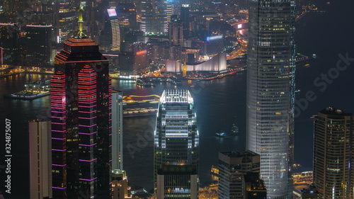 Photography Hong Kong city skyline timelapse at night with Victoria Harbor and skyscrapers illuminated by lights over water viewed from mountain top