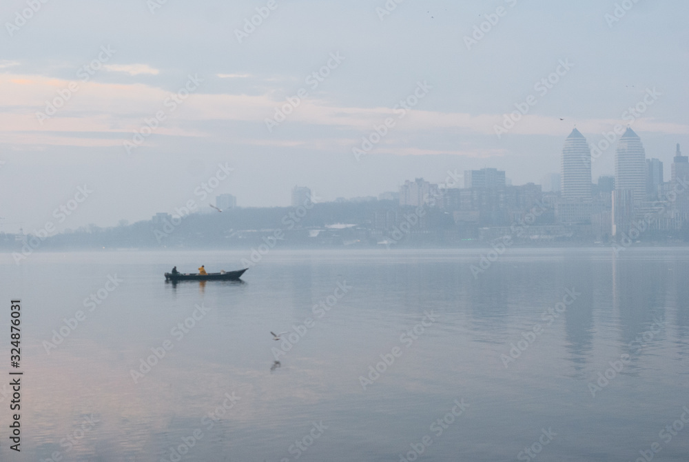 Fishing boat on the Dnieper river against the background of silhouettes of urban buildings.