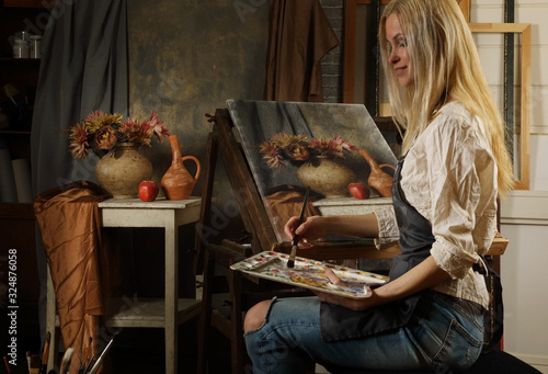 Young adult female artist paints an oil painting