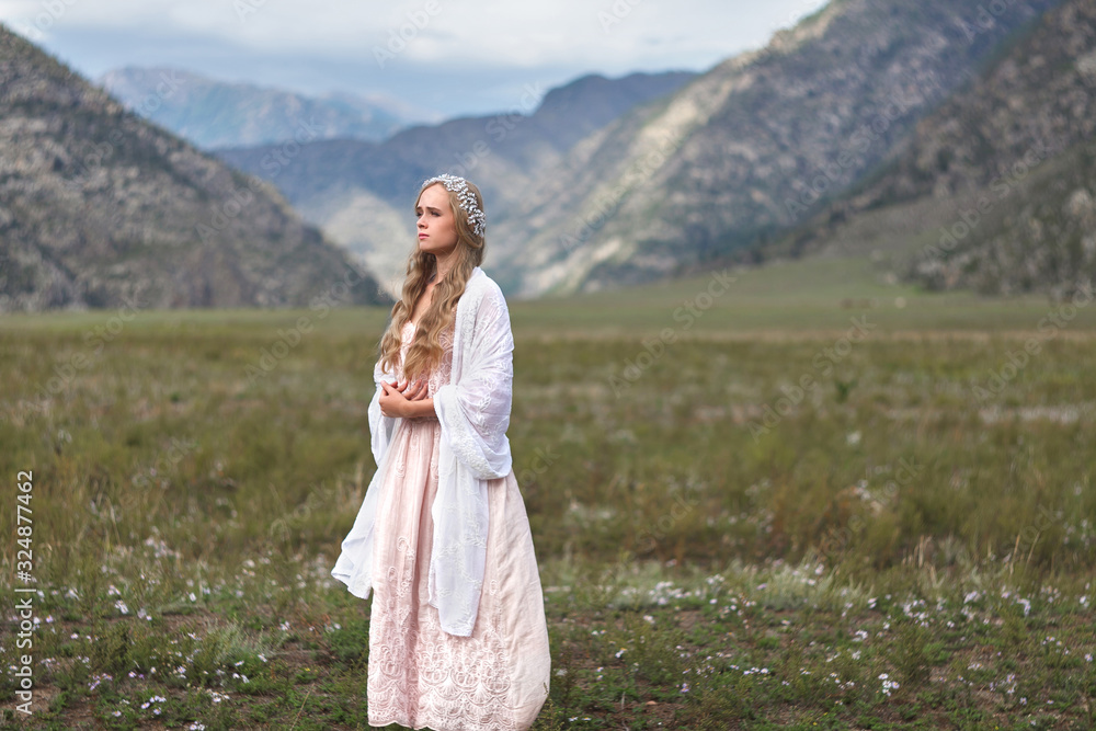 A girl walks through the meadow against the backdrop of the mountains. Prayer.