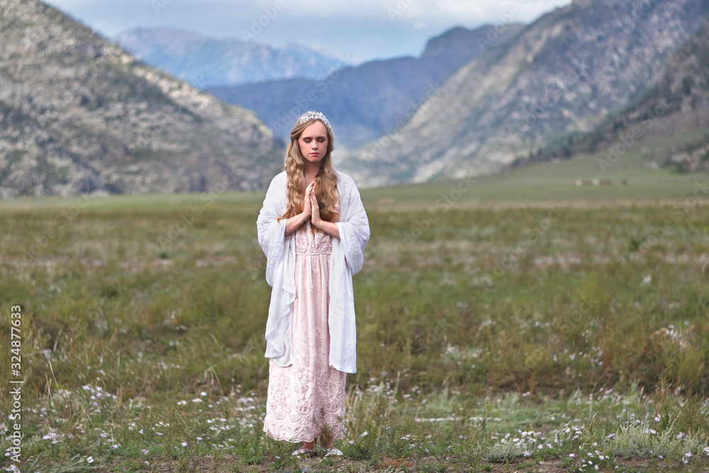A girl walks through the meadow against the backdrop of the mountains. Prayer. A girl walks through the meadow against the backdrop of the mountains. Prayer.