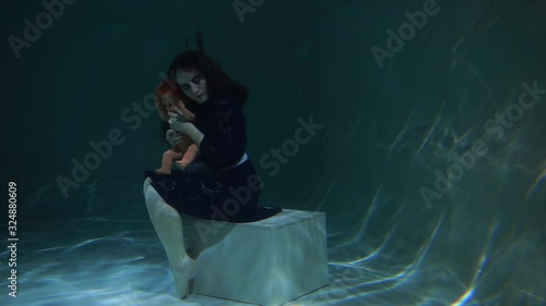 Beautiful and cute girl swims underwater in the pool with her doll. Disappointment and sadness. Long hair and blue dress. Water and the ocean. Fairy tale