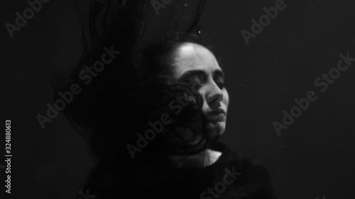 A brunette girl underwater looks at the camera and her hair develops. Mermaid and Nymph. Beautiful girl in the pool. Long hair.