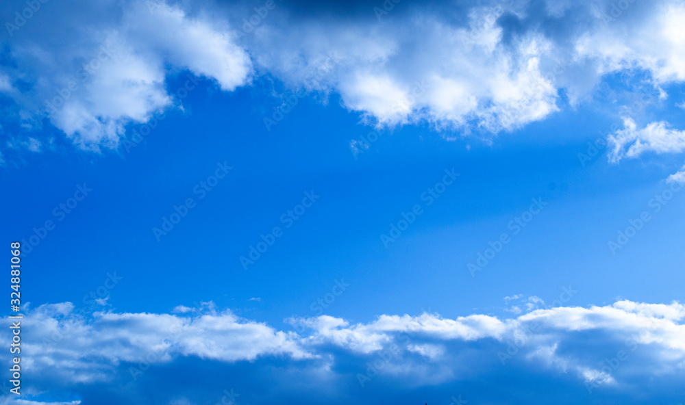 Fototapeta premium Blue sky with clouds on the top and the bottom of the composition and free space in the centre.