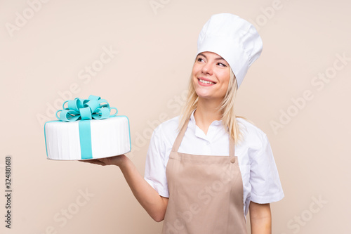 Young Russian woman with a big cake over isolated background looking up while smiling