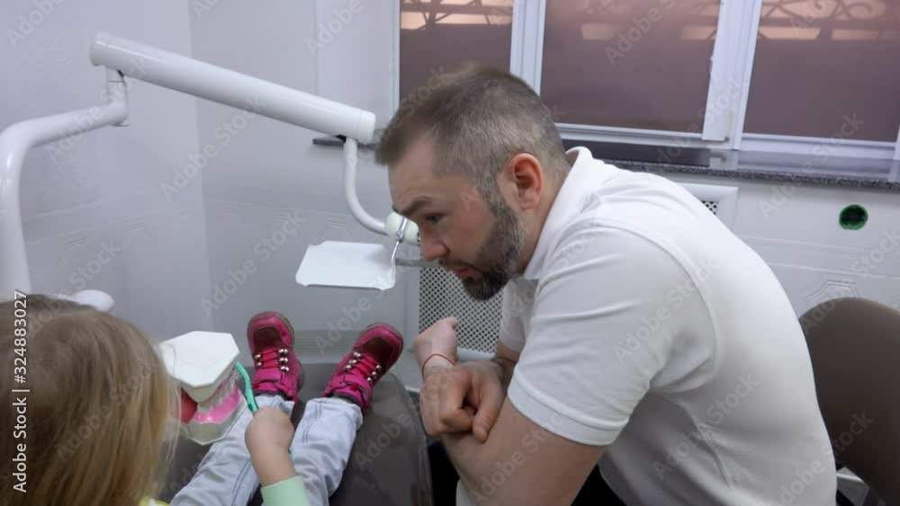 Dentist explains to a little cute girl how to clean her teeth with a teeth brush on a jaw model Dentist explains to a little cute girl how to clean her teeth with a teeth brush on a jaw model