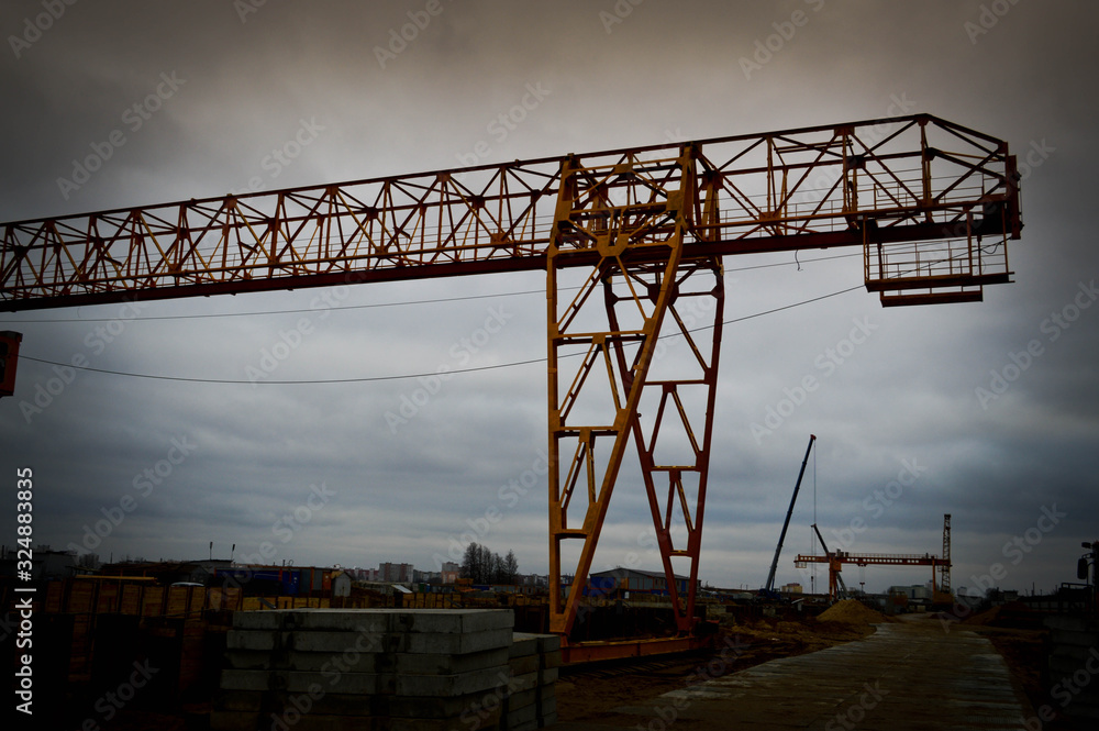 High heavy yellow metal iron load-bearing construction stationary industrial powerful gantry crane of bridge type on supports for lifting cargo on a modern construction site of buildings and houses