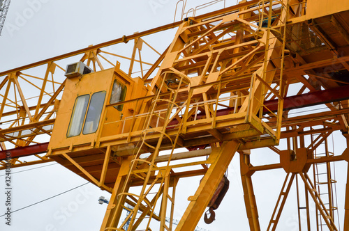High heavy yellow metal iron load-bearing construction stationary industrial powerful gantry crane of bridge type on supports for lifting cargo on a modern construction site of buildings and houses