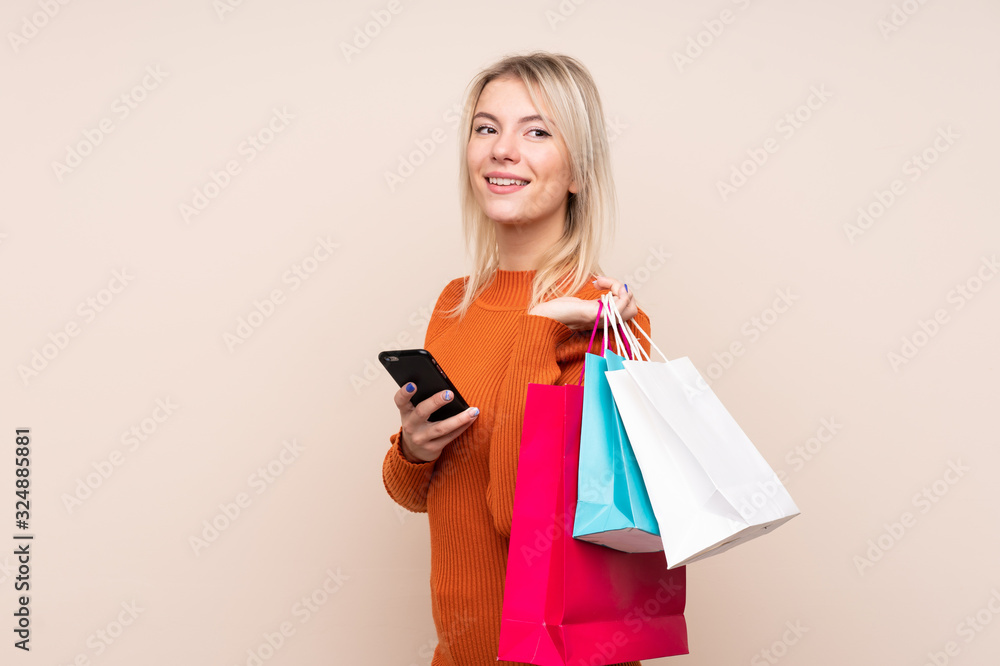 Young blonde woman over isolated background holding shopping bags and a mobile phone