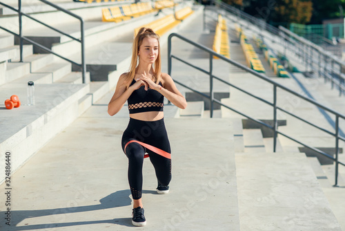 Young sporty woman doing exercises with rubber band outdoor