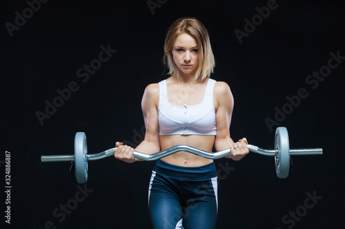 Close-up portrait of a fitness Muscular young girl posing with curly barbell at the gym isolated on a black background © satyrenko