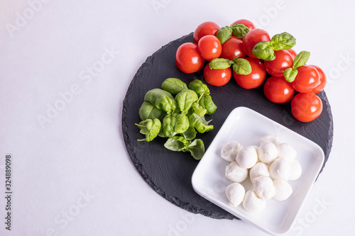 mozzarella in a cup, basil and tomatoes on a stone tile