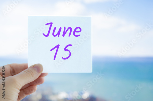 June 15th. Hand holding sticker with text June 15 on the blurred background of the sea and sky. Copy space for text. Month in calendar concept
