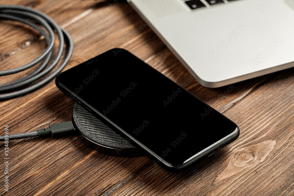 Wireless charging lies next to the computer on a stylish wooden table Wireless charging lies next to the computer on a stylish wooden table