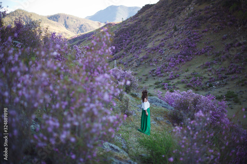 A girl walks in bloom of flowers against the backdrop of a mountain landscape.