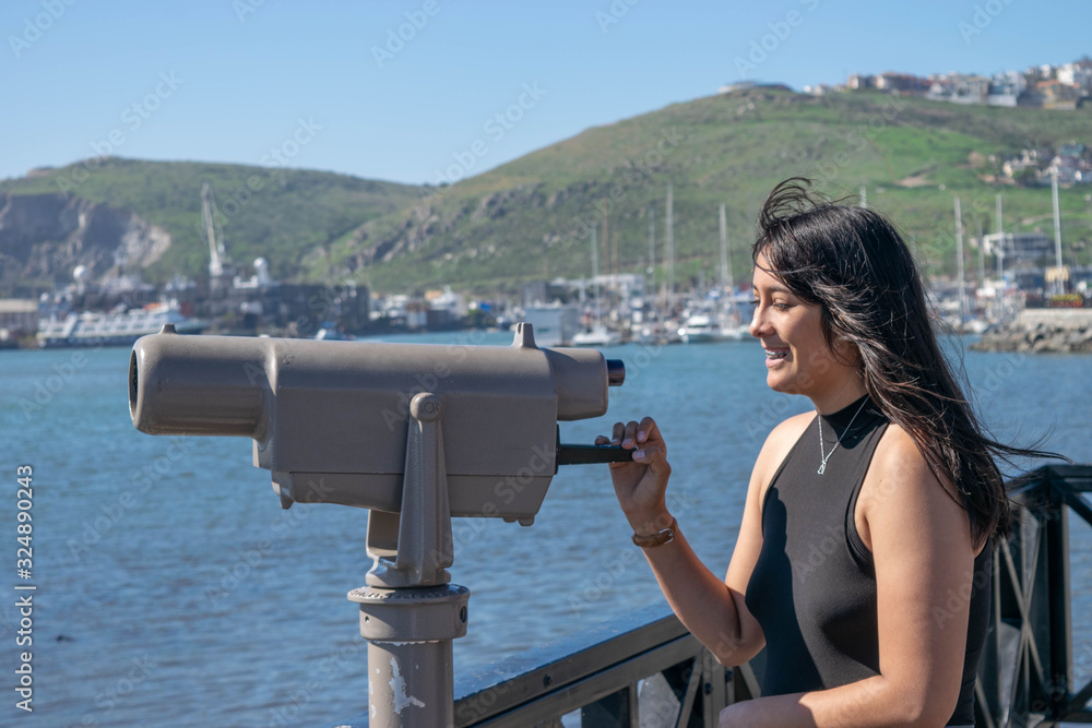 beautiful mexican girl playing with telescope on the pier in front of the sea