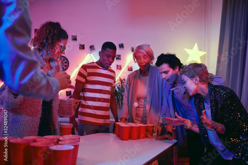 Group of people of different ages playing together in beer pong game during home party