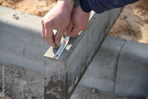 A worker measures a concrete block with a ruler, close-up.