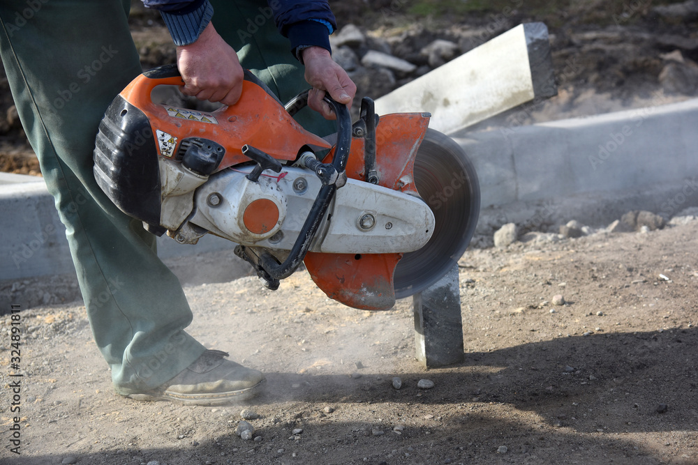 A worker saws a concrete block with a circular saw and builds a pedestrian road.