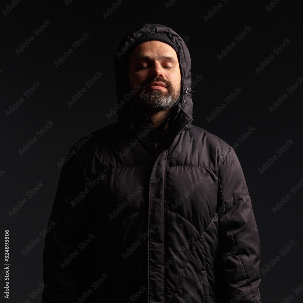 Portrait of a man in a hooded jacket. Studio shooting, dark background.