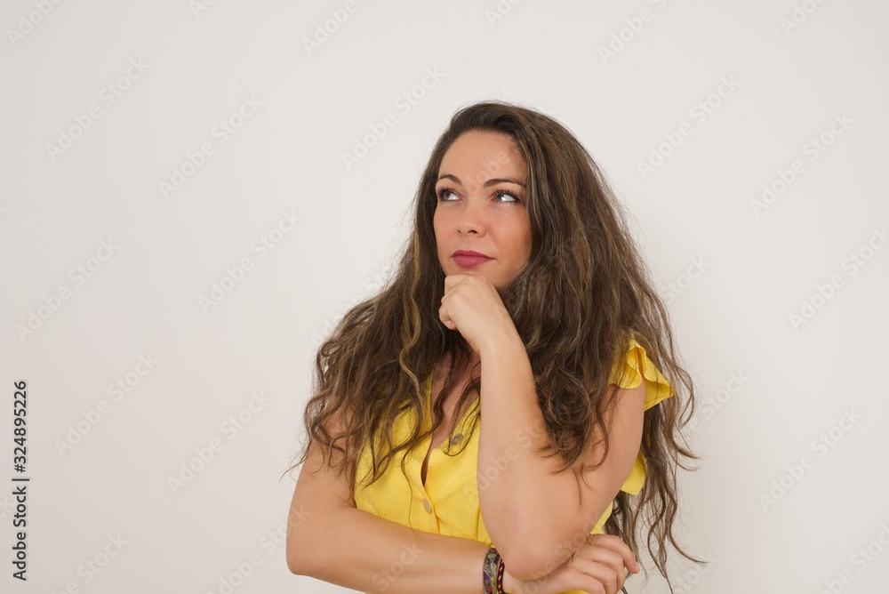 © Jihan - Portrait of thoughtful smiling girl keeps hand under chin, looks sideways, thinking or wondering about something with interest, dressed casually, poses against gray studio. Taking decisions concept.