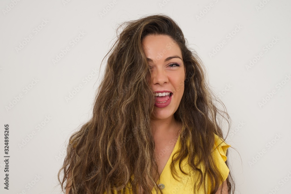 Horizontal portrait of pleasant-looking Caucasian female with long beautiful hair wearing brown sweater covering her face with hair looking happily to the camera.