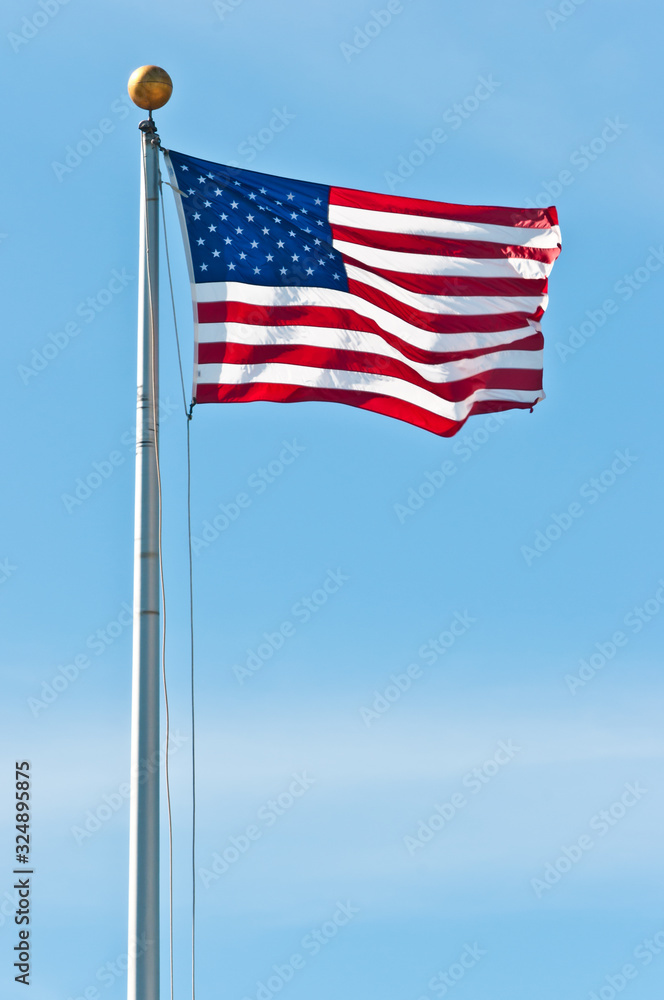 Front view, far distance of the american flag, fluttering in the breeze on a tall aluminum pole with a blue sky Front view, far distance of the american flag, fluttering in the breeze on a tall aluminum pole with a blue sky