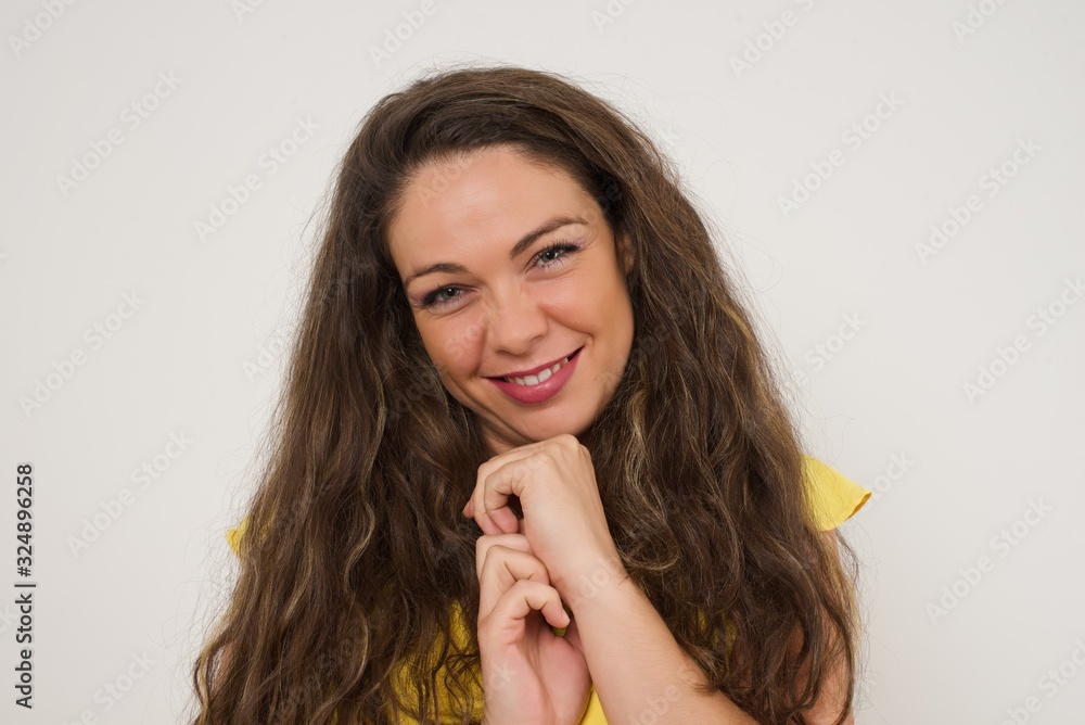 Dreamy charming young female with pleasant expression, keeps hands crossed near face, excited about something pleasant, poses against gray background. Dreamy charming young female with pleasant expression, keeps hands crossed near face, excited about something pleasant, poses against gray background.