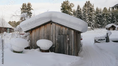 Winter landscape. Exterior view of wooden house covered with snow in Russian village located in Siberia. Russia. 4K photo