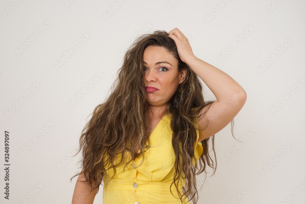 Oops, what did I do? Beautiful blonde woman holding hand on head with frightened and regret expression. Wearing casual clothes standing against gray background.