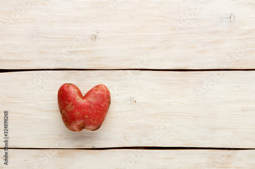 Ugly potato in the heart shape on a white wooden background. Vegetable or food waste concept. Top view, close-up.