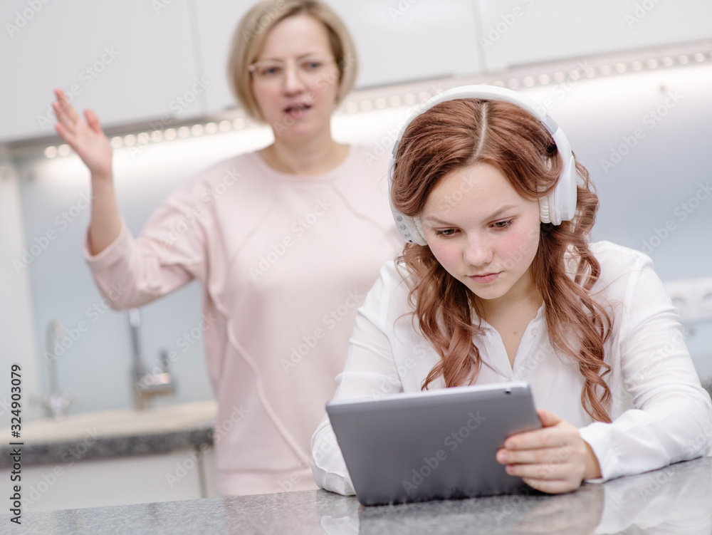 Mom scolds yelling at a teenager girl The girl does not respond to her mother and continues to look at the screen of a tablet computer. Relationship problems, puberty probl Mom scolds yelling at a teenager girl The girl does not respond to her mother and continues to look at the screen of a tablet computer. Relationship problems, puberty probl