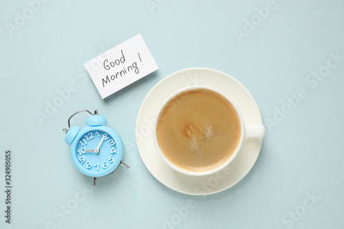 Delicious coffee, alarm clock and card with GOOD MORNING wish on light background, flat lay