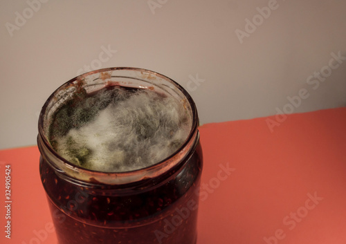 White and gray moldіness in a jar on raspberry jam. Photo from the top on a white and pink background