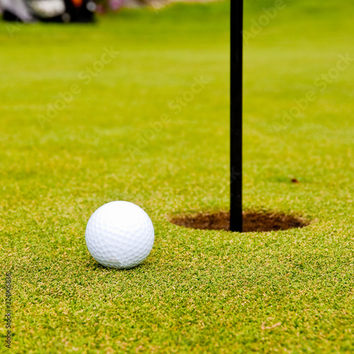 Golf ball on green with flag. Shallow depth of field. Focus on the ball.