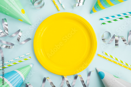 Birthday, party and holiday concept. Festive caps, streamer, drinking straws and bright paper plate on light blue background. Top view, flat lay, copy space
