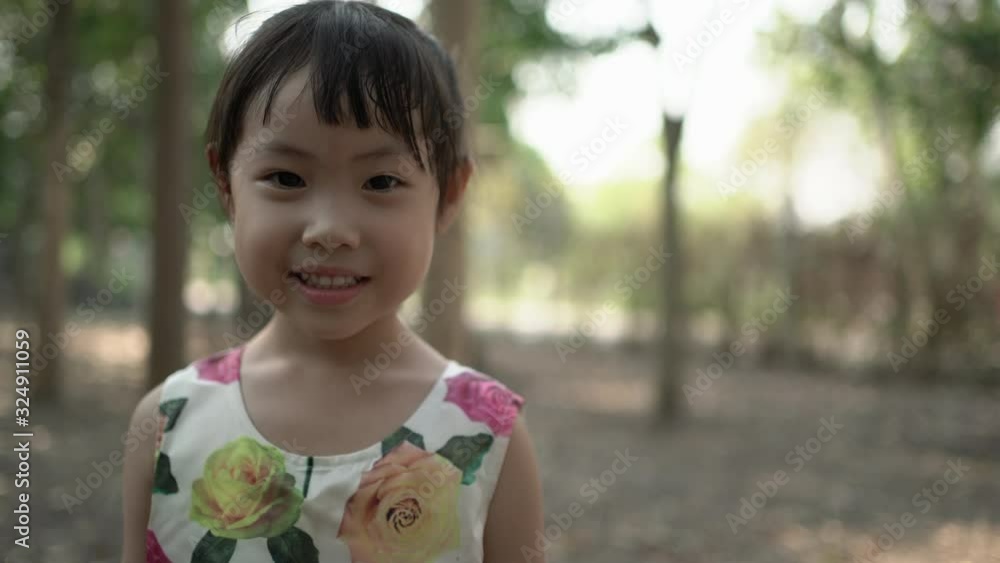 Little asian girl smiling and looking at camera. Little girl in the garden. Handheld shot Little asian girl smiling and looking at camera. Little girl in the garden. Handheld shot