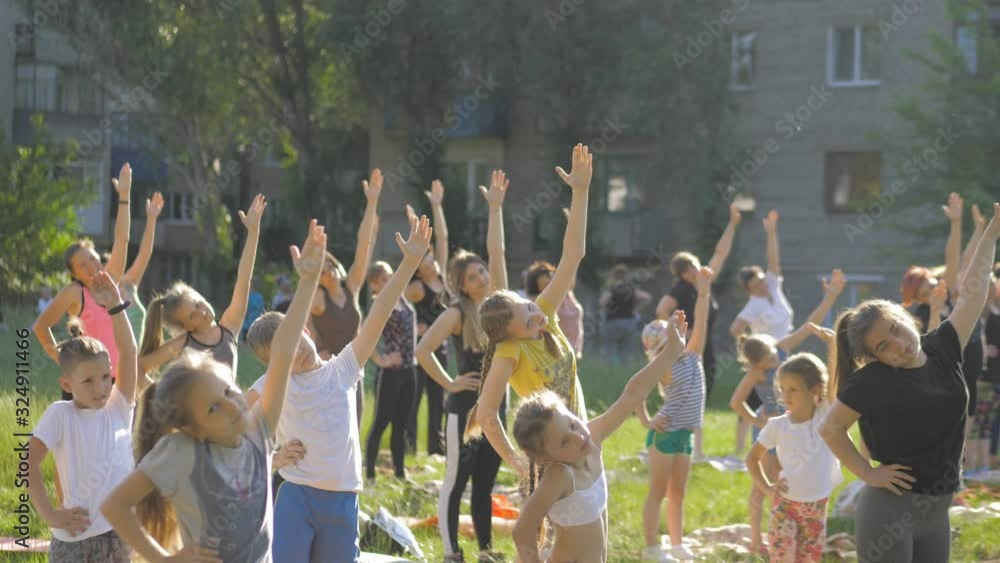 Big group of adults and kids attending a yoga class outside in park Big group of adults and kids attending a yoga class outside in park