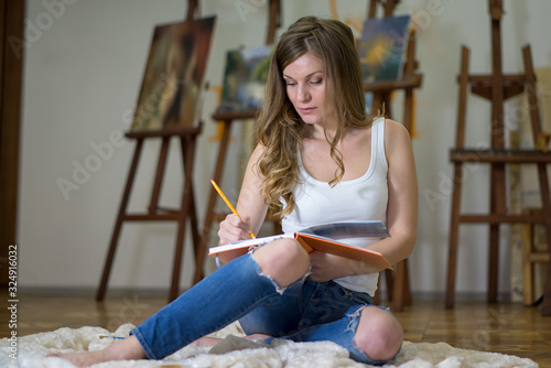 Portrait of a woman artist sitting on the floor and painting in the art studio.