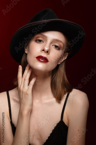 Portrait of beautiful girl  in black clothes and a hat with space for text. Young cute brunette on a dark red background. Fashion, beauty, makeup, cosmetics. © kiy_lg