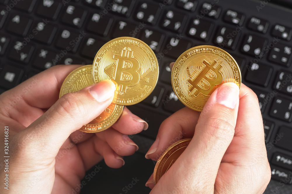 Woman hand holding golden coloured bitcoin coin over black laptop keyboard Woman hand holding golden coloured bitcoin coin over black laptop keyboard