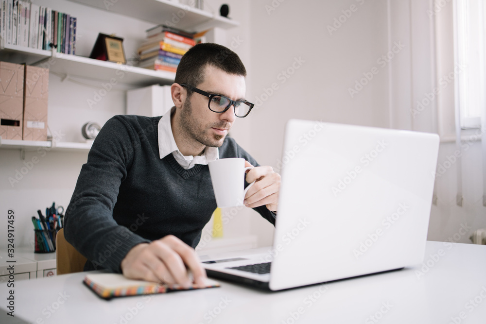 Employee holding white mug while using laptop Employee holding white mug while using laptop