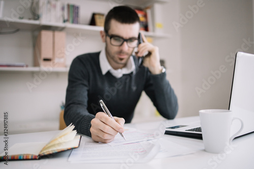 Blurred man talking on phone and sitting on desk with documents