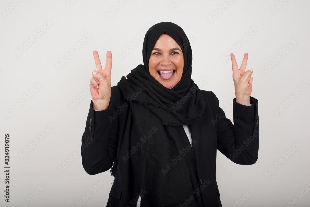 Indoor portrait of young caucasian female isolated on gray background with optimistic smile, showing peace or victory gesture with both hands, looking friendly. V sign. Indoor portrait of young caucasian female isolated on gray background with optimistic smile, showing peace or victory gesture with both hands, looking friendly. V sign.