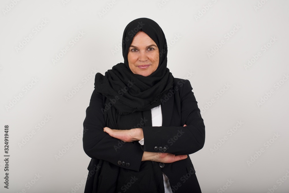 Waist up shot of beautiful self confident cheerful muslim woman entrepreneur has broad smile, crosses arms, happy to meet with colleague, dressed in fashionable clothes. Waist up shot of beautiful self confident cheerful muslim woman entrepreneur has broad smile, crosses arms, happy to meet with colleague, dressed in fashionable clothes.