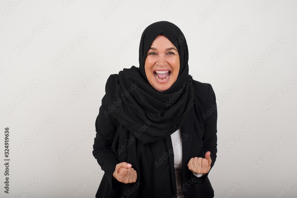 Close up portrait of stylish muslim lady with wave hairstyle raising fists up isolated on shine grey background big eyes and wide open mouth. Close up portrait of stylish muslim lady with wave hairstyle raising fists up isolated on shine grey background big eyes and wide open mouth.